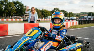Un enfant d'environ 8 ans portant un casque de sécurité et souriant au volant d'un karting adapté sur une piste extérieure, avec un parent encourageant en arrière-plan sous un soleil doux de Vendée.