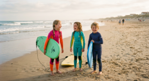 De jeunes enfants en combinaison de surf sourient sur la plage avec leurs planches, dans une ambiance chaleureuse et sécurisante.