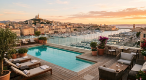 Vue panoramique depuis la terrasse d'un hôtel moderne sur le Vieux-Port de Marseille avec une piscine en premier plan à l'heure dorée.