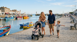 Une famille se promène avec une poussette sur un quai ensoleillé à Saint-Gilles-Croix-de-Vie, entre les bateaux de pêche et l'océan.