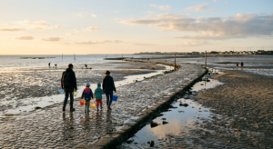 Paysage du Passage du Gois à marée basse avec des familles pêchant à pied sous un ciel de fin de journée doux.