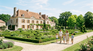 Vue extérieure d'un logis historique en pierre avec son jardin à la française, une famille marche tranquillement sur le chemin, ambiance ensoleillée et paisible en Vendée.