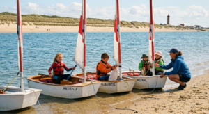 Enfants en gilets de sauvetage apprenant l'optimist sur une plage ensoleillée de Vendée, ambiance douce et familiale.