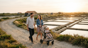 Une famille se promène avec une poussette sur un sentier plat bordant les marais salants de l'Île-d'Olonne sous une lumière douce de fin de journée.
