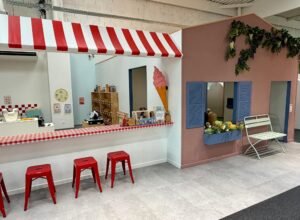 Vue chaleureuse d'un espace de jeu d'imitation en bois dans un parc indoor lumineux à Nîmes, style ludo-éducatif.