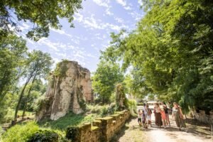 Une famille avec enfants explorant avec enthousiasme le domaine boisé du Château des Essarts, entre ruines historiques et forêt verdoyante.