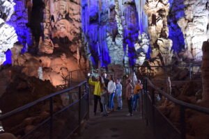 Intérieur spectaculaire de la Grotte de la Salamandre avec des stalactites géantes éclairées de manière magique et une famille observant le spectacle depuis un belvédère.