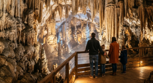 Intérieur spectaculaire de la Grotte de la Salamandre avec des stalactites géantes éclairées de manière magique et une famille observant le spectacle depuis un belvédère.
